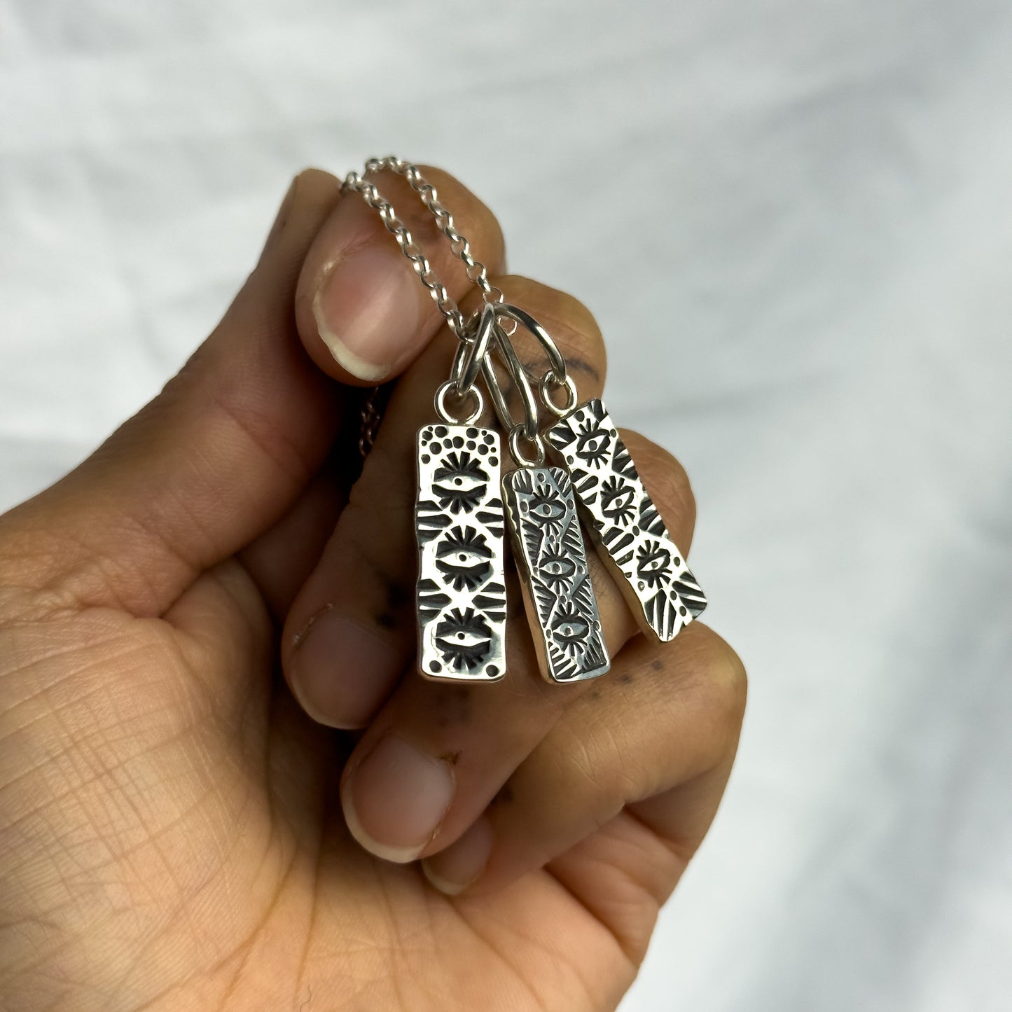 Hand holding a silver necklace with two pendant tags against a white background
