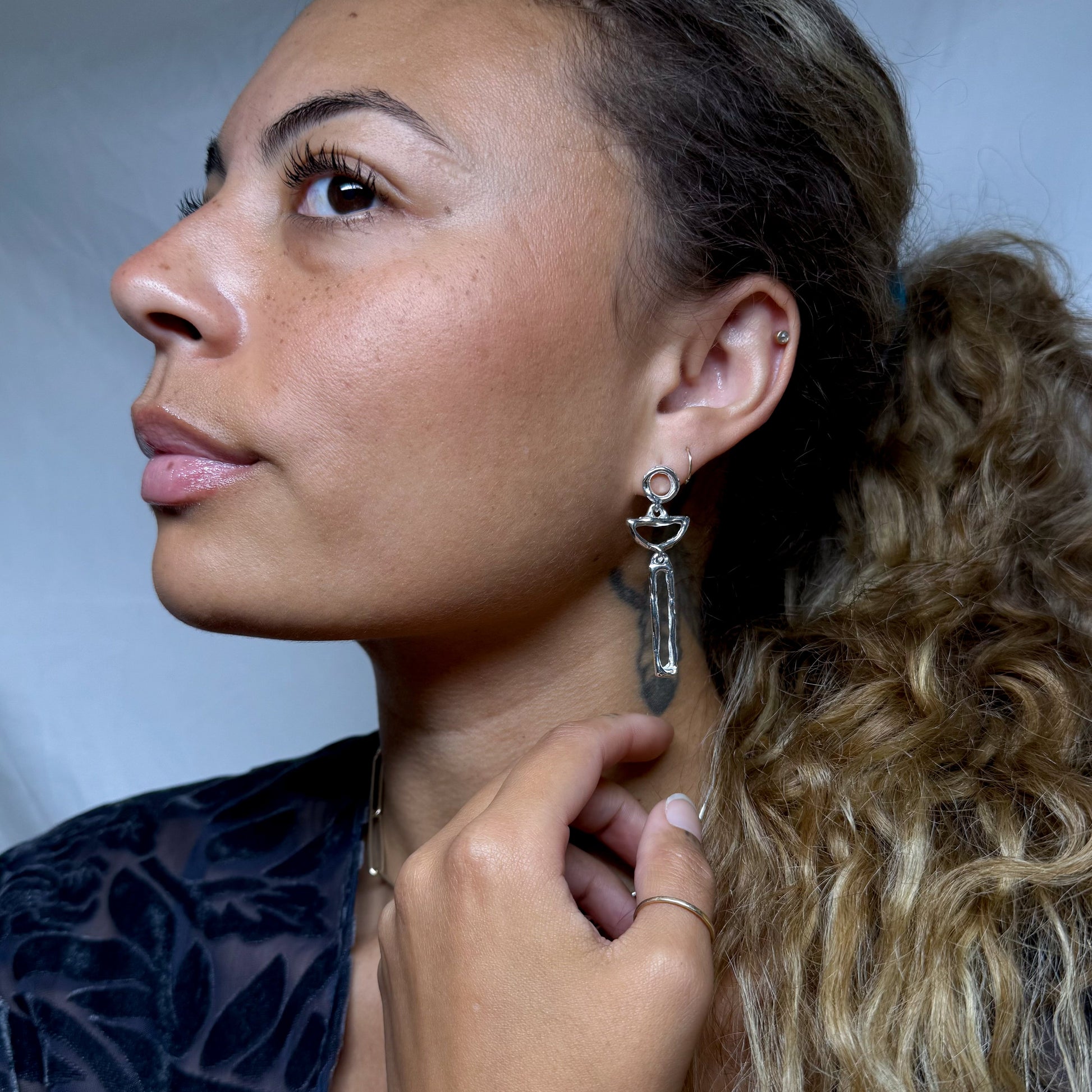 Woman adjusting an earring with a neutral background