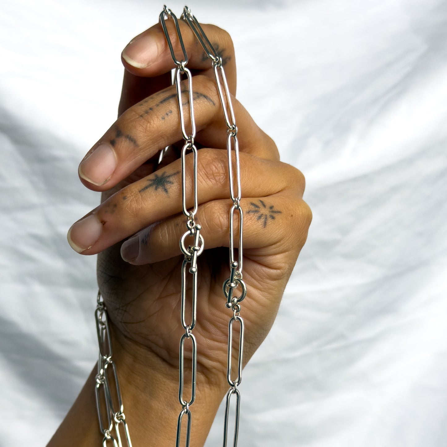 Hand holding a silver chain necklace against a white background