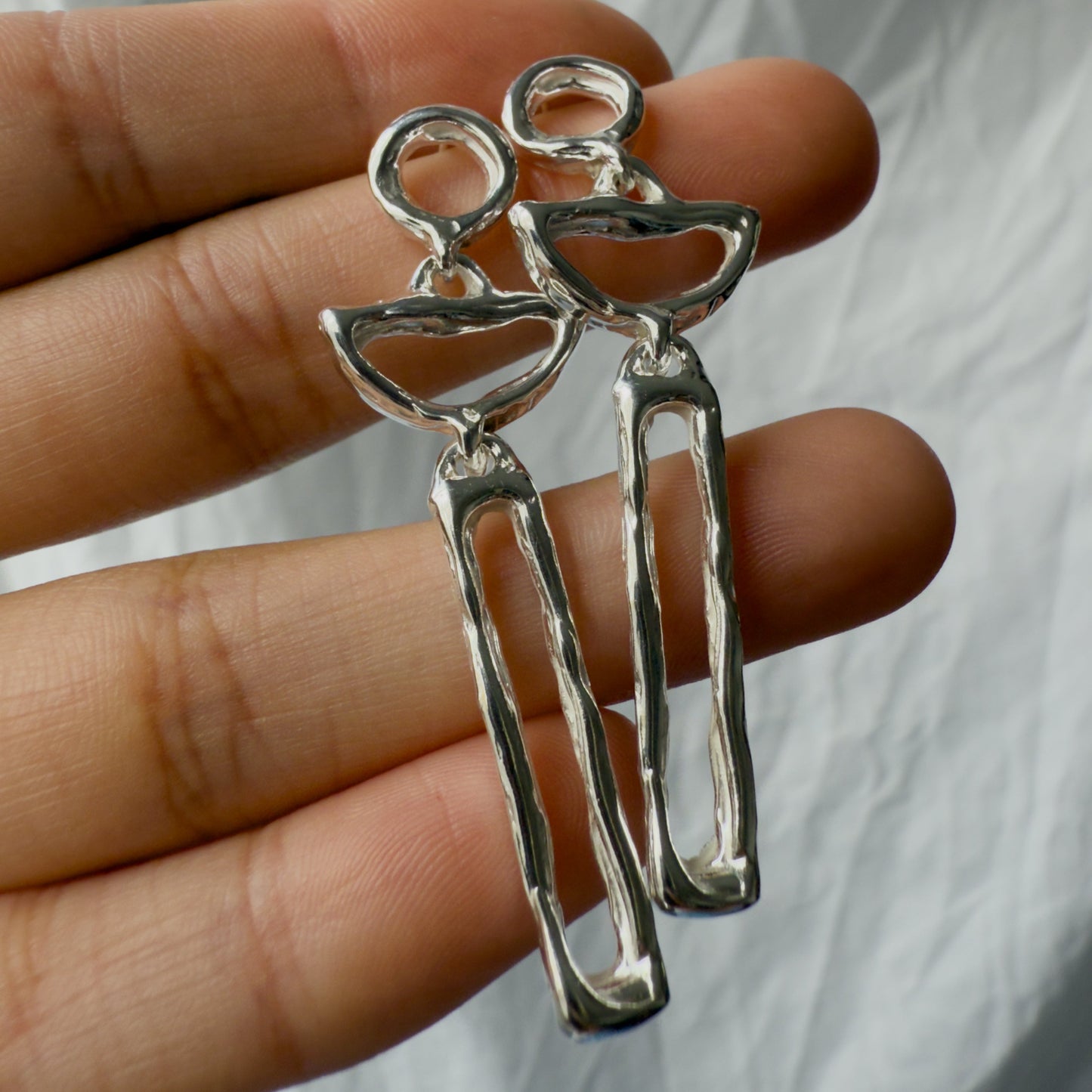 moon shaped earrings held between fingers against a neutral background