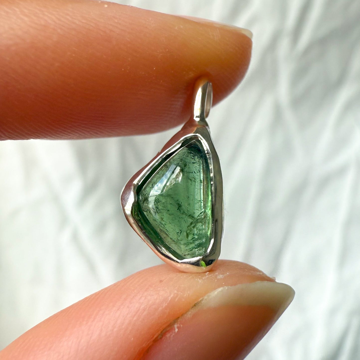 Green tourmaline stone pendant held between two fingers against a white background