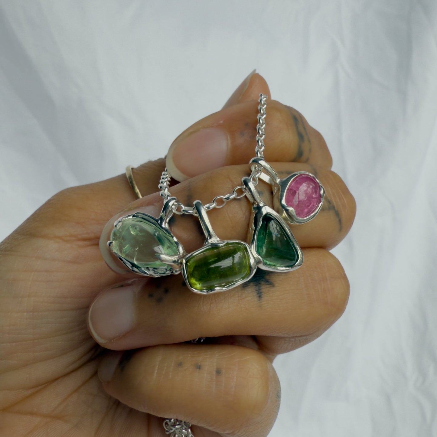 Hand holding a silver necklace with green and pink tourmaline gemstones against a white background