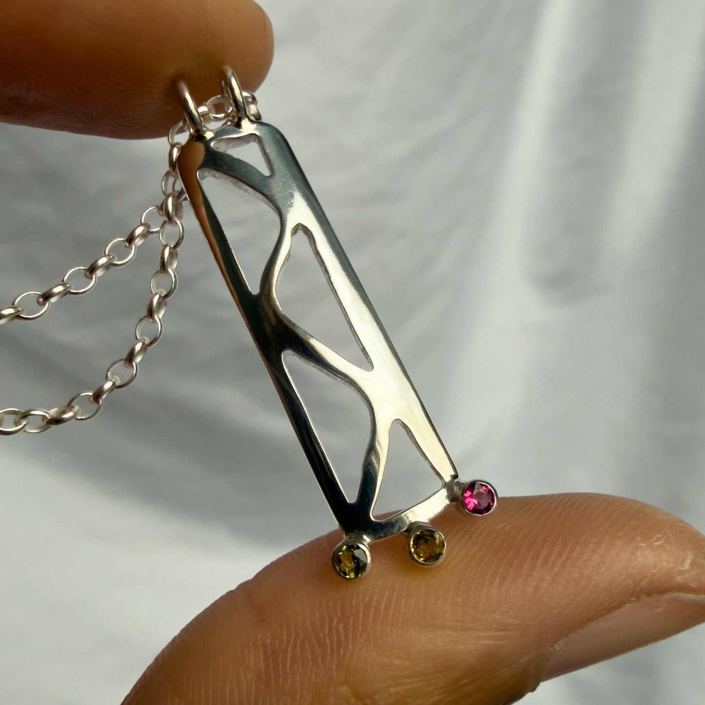 silver necklace with a pink gemstone held by a hand against a white background