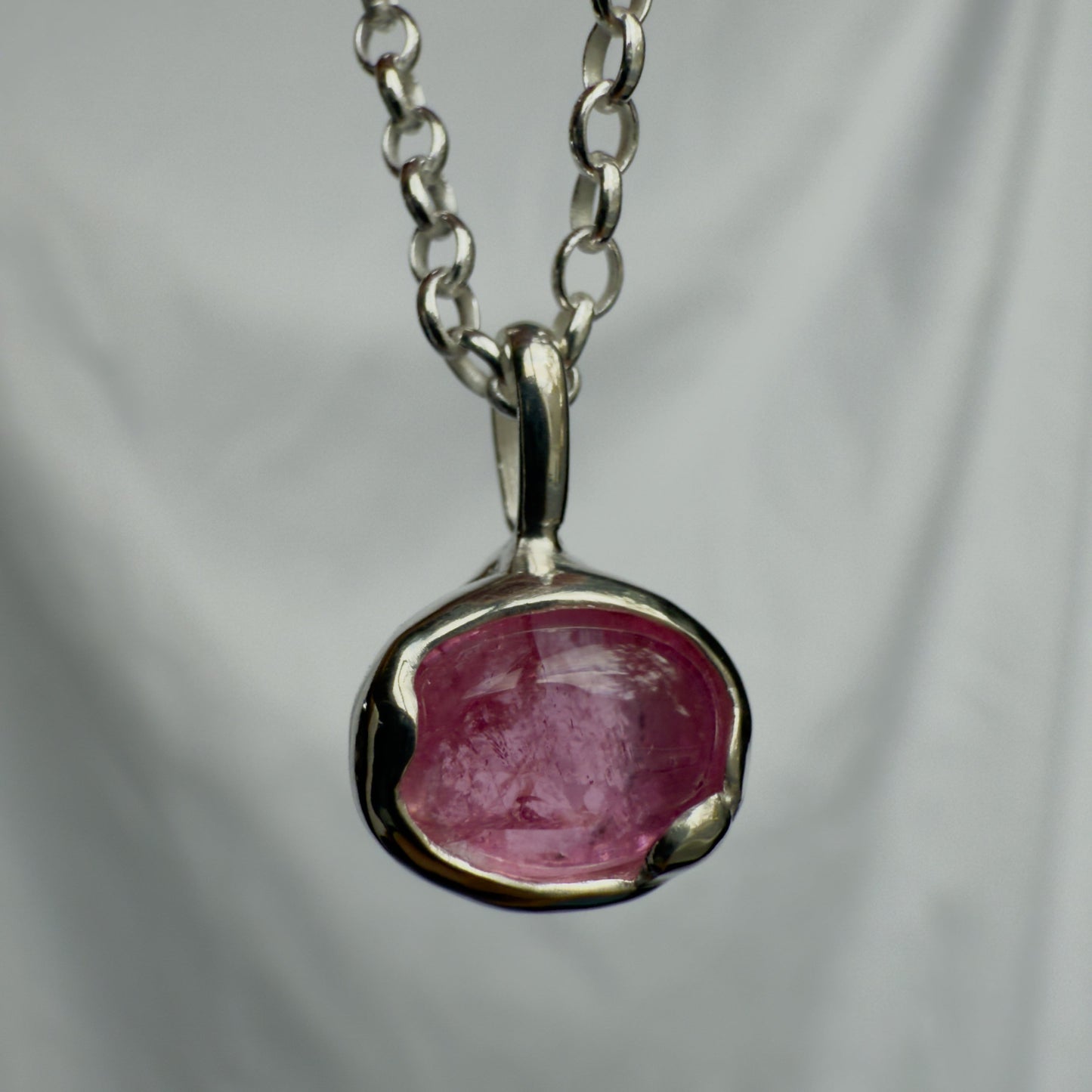 Silver pendant with a pink tourmaline stone on a chain against a gray background