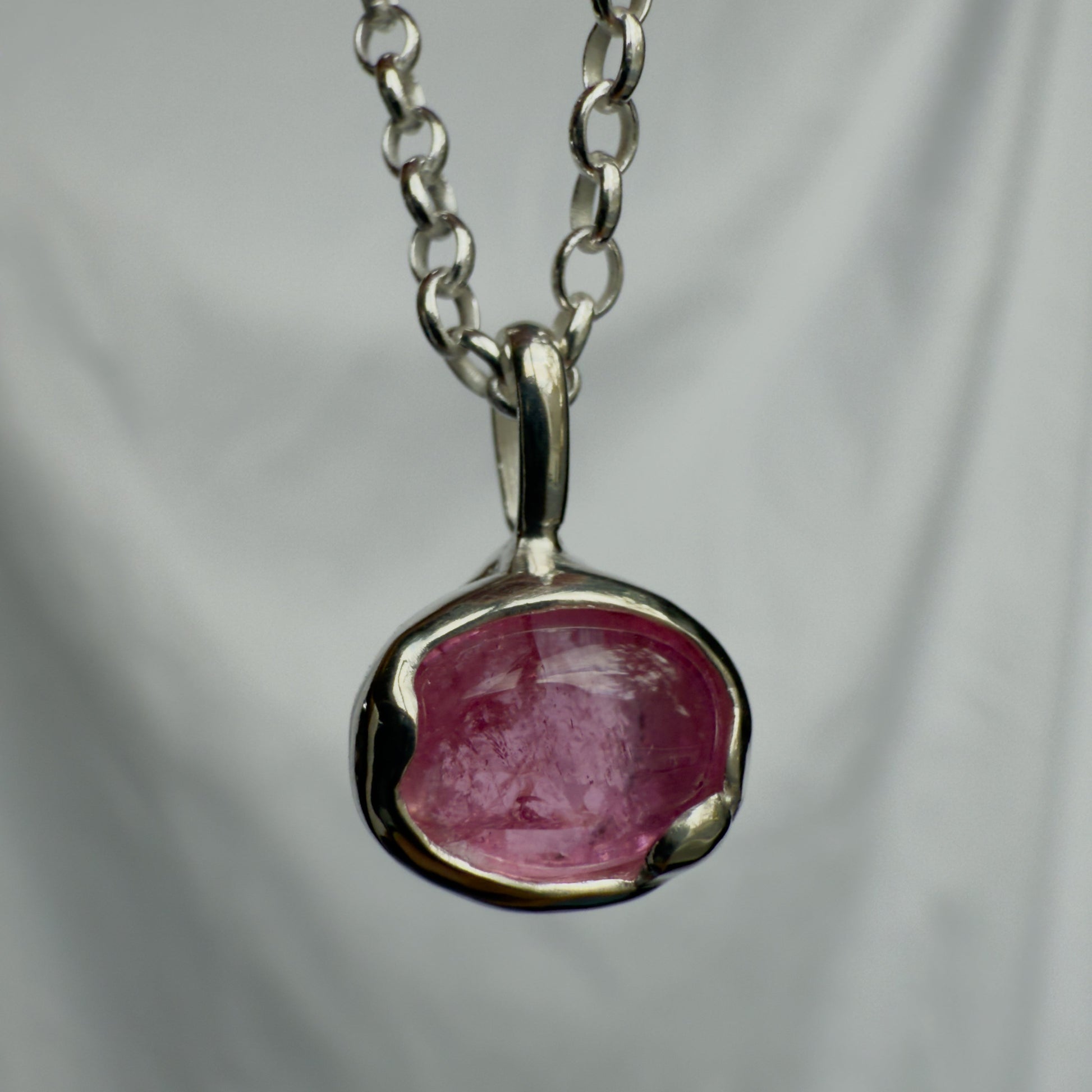 Silver pendant with a pink tourmaline stone on a chain against a gray background