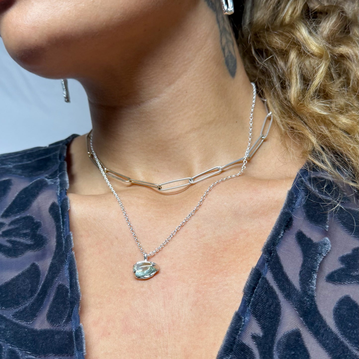 Close-up of a person wearing silver earrings and necklaces with green tourmaline.